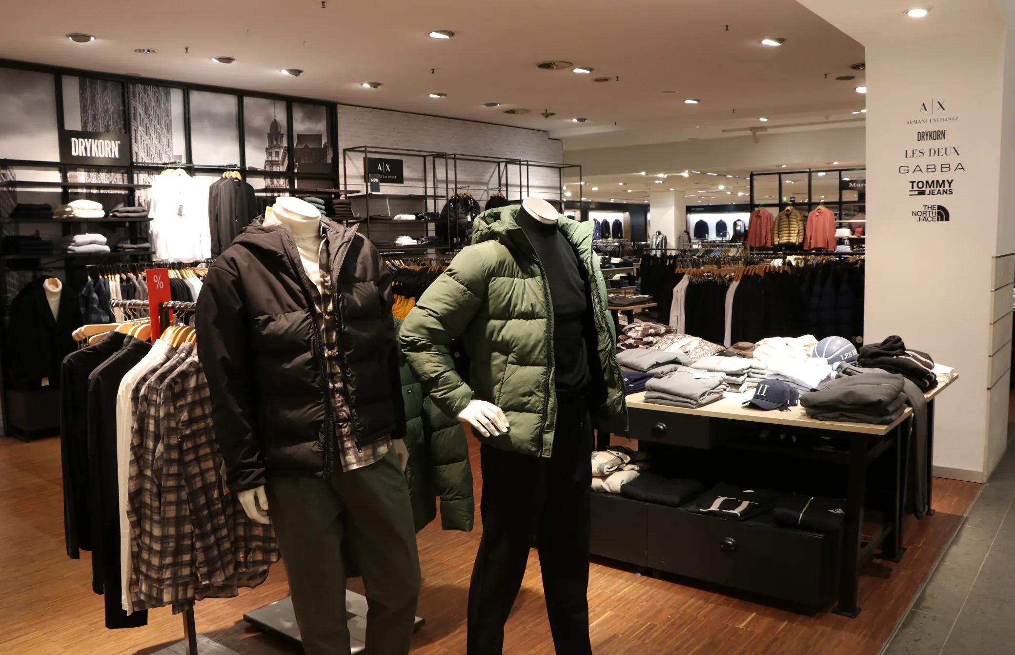 Men's clothing store with mannequins in winter jackets and folded clothes on display tables.
