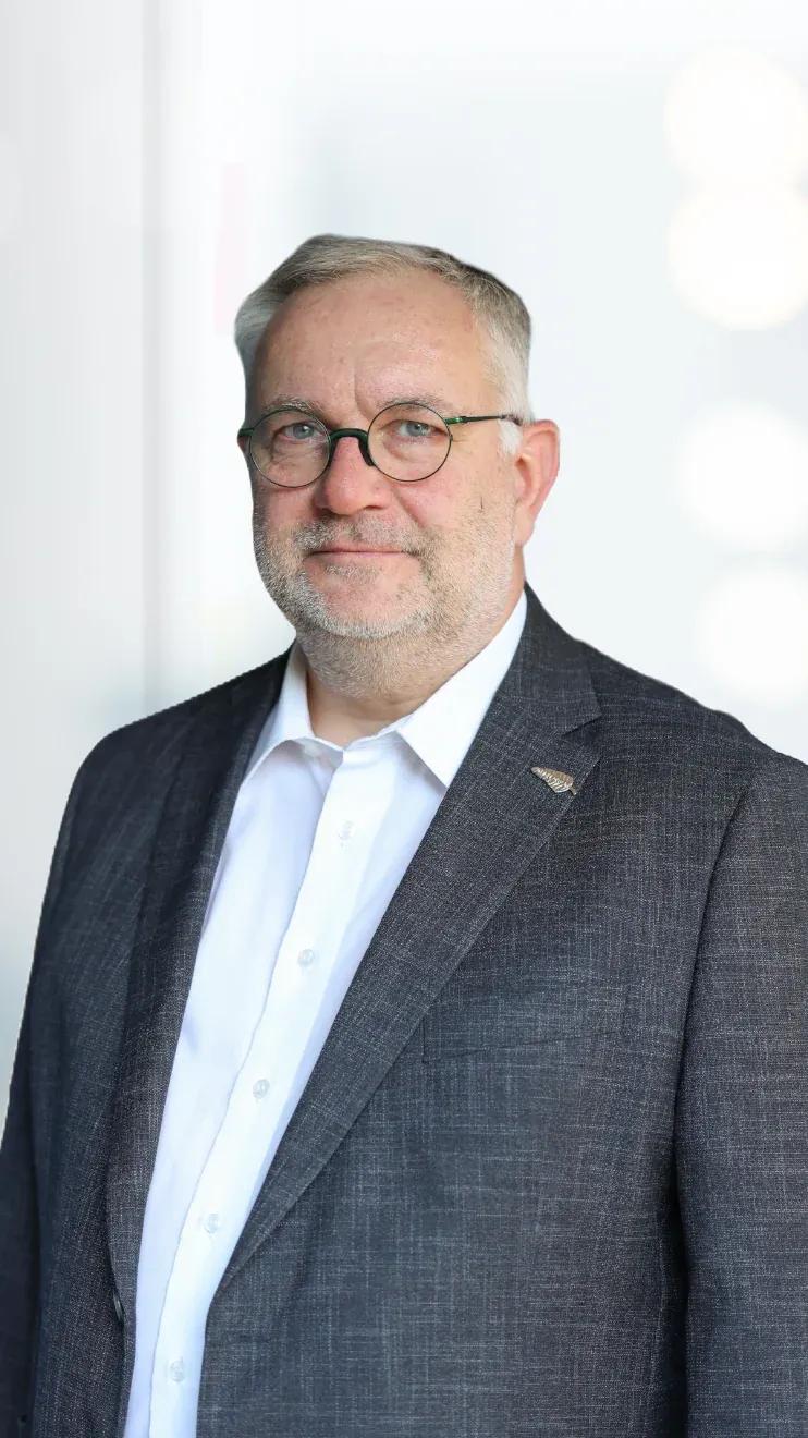 Portrait of a middle-aged man with glasses wearing a suit, looking at the camera.